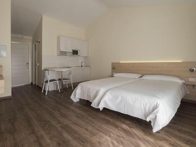 Camera d'hotel luminosa con letto matrimoniale, scrivania e pavimento in legno.