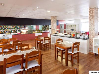 Modern eingerichteter Frühstücksraum mit Holztischen, Stühlen und langer Theke im Hintergrund.