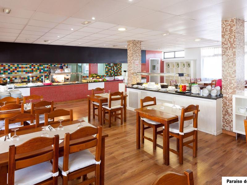 Sala colazione luminosa con tavoli e sedie in legno, area buffet ed elementi decorativi moderni.