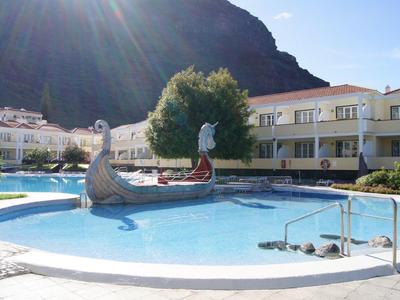 Round pool with water feature in front of hotel and rocky hill in background.