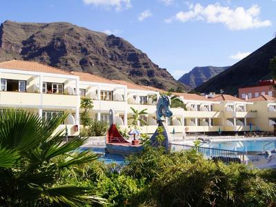 Hotel with pool in front of mountains and lush vegetation under sunny sky