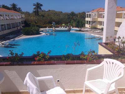 Hotelpool mit umliegenden Gebäuden, weißen Stühlen und Balkon mit Blick auf den Pool.