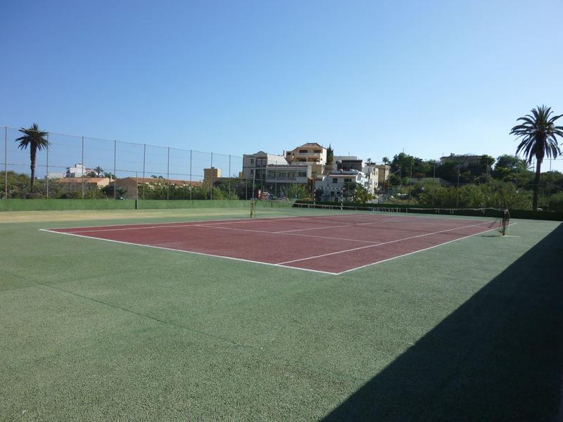 Outdoor tennis court with red playing area and green border under clear sky