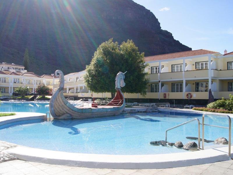 Round pool with water feature in front of hotel and rocky hill in background.
