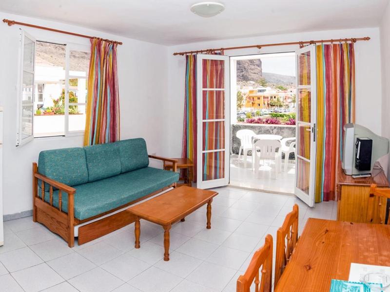Bright living room with sofa, wooden table, dining table, and balcony door overlooking the mountains.