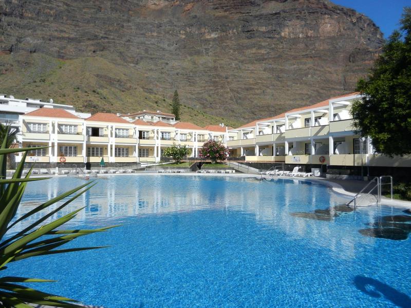Large hotel with pool in front of rocky mountain and clear blue sky.