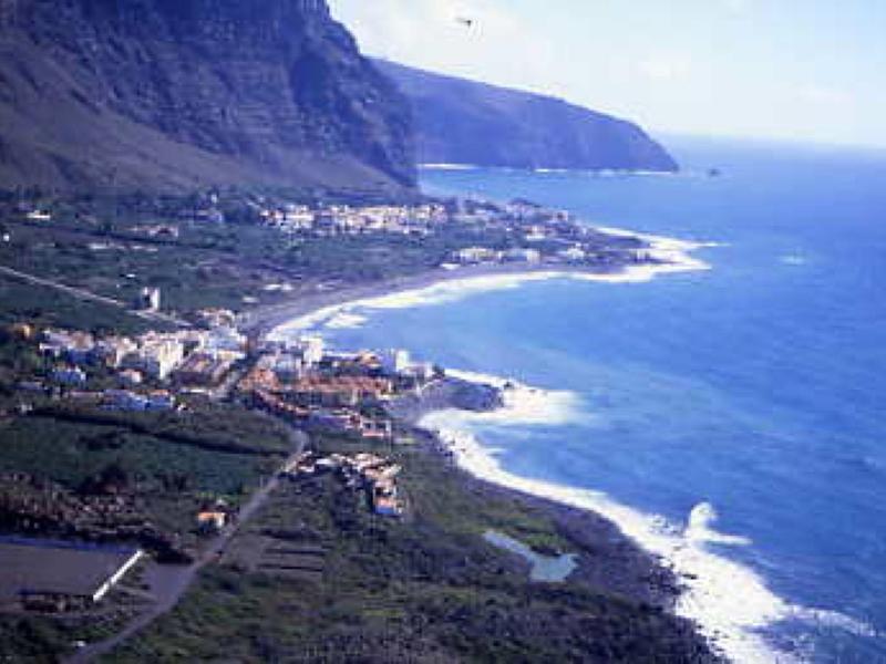 Modern white hotel building with balconies and palm trees in a tropical setting.