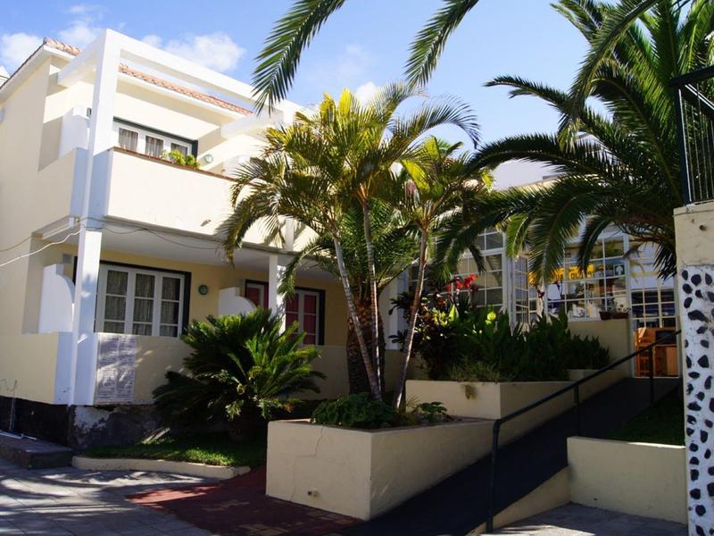 Modern white hotel building with balconies and palm trees in a tropical setting.