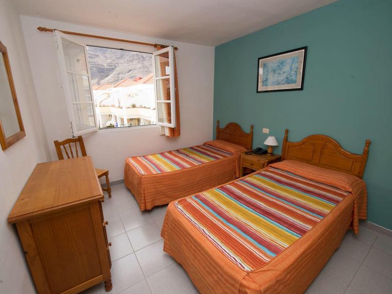 A simple hotel room with two single beds, a wooden desk, and a window overlooking outside.