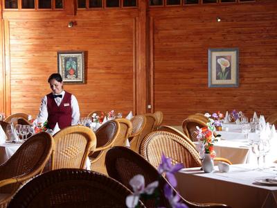 Restaurant mit Holzwänden, geflochtenen Stühlen, gedeckten Tischen und einem Kellner im Hintergrun