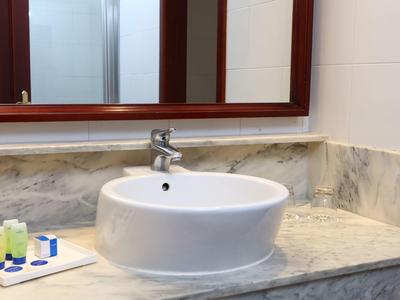 Weißes rundes Waschbecken auf Marmorwaschtisch mit Spiegel und kleinen Toilettenartikeln.