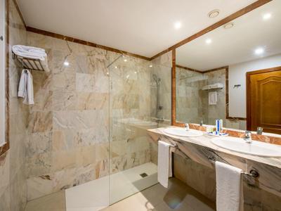 Helles Badezimmer mit Marmorfliesen, großer Spiegelwand, Doppelwaschbecken und Glas-Dusche.
