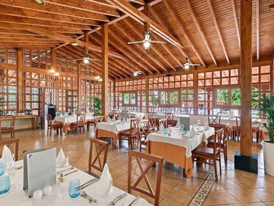 Licht restaurant met houten balkenplafond, houten tafels, stoelen en grote ramen.