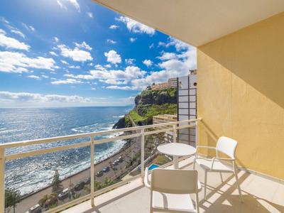 Balkon met stoelen en tafel met uitzicht op zee en bewolkte lucht.