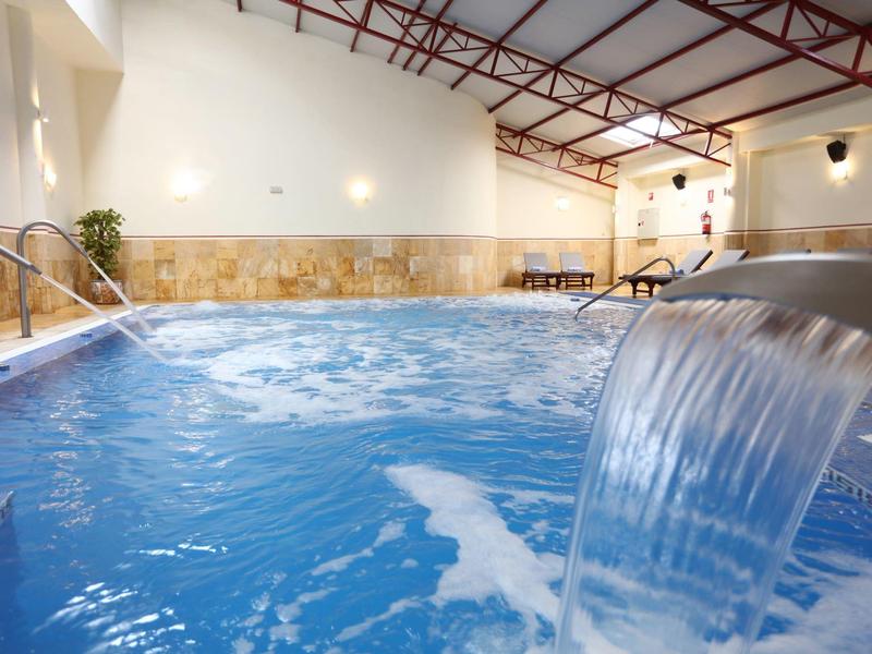 Overdekt zwembad met waterval en ontspannen sfeer in een hotelspa.