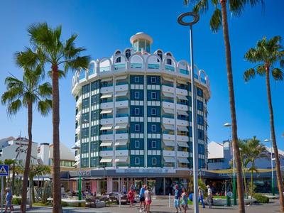 Edificio rotondo di un hotel con finestre blu e palme in primo piano sotto un cielo sereno.