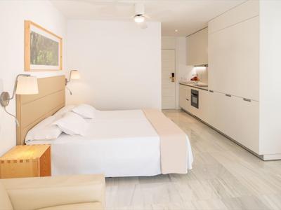 Camera d'hotel luminosa con letto matrimoniale, angolo cottura e interni moderni.