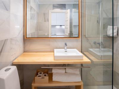 Bagno moderno con lavabo su piano in legno, WC e doccia con parete in vetro.