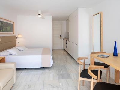 Camera d'hotel luminosa con letto, scrivania, sedie e angolo cottura.