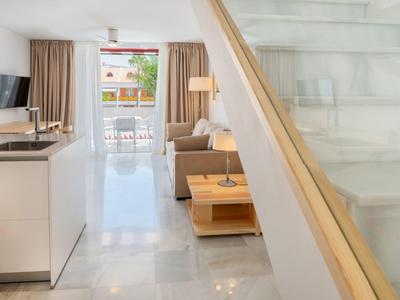 Soggiorno luminoso con divano, lampada e grande finestra con vista sulla terrazza.