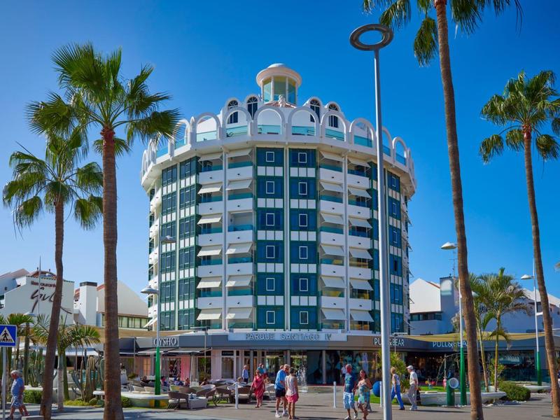Edificio rotondo di un hotel con finestre blu e palme in primo piano sotto un cielo sereno.
