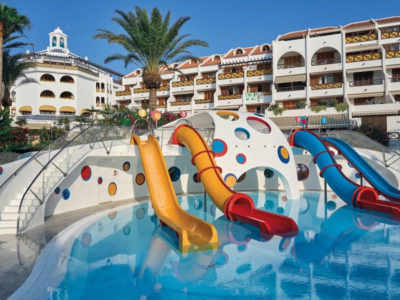 Scivoli d'acqua colorati in una piscina davanti a un hotel con palme.