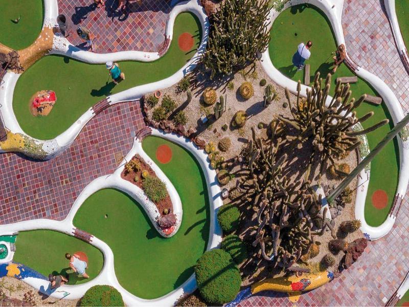 Vista aerea di un campo da mini golf colorato circondato da attività estive affollate.