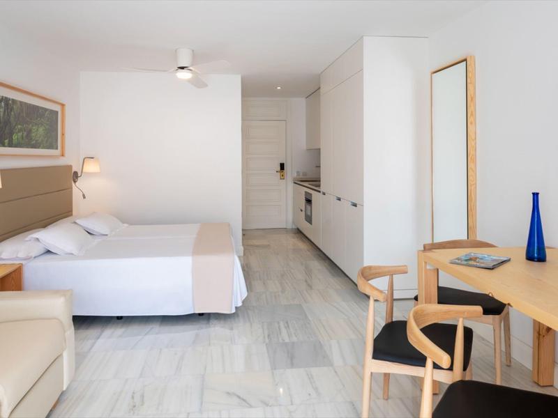 Camera d'hotel luminosa con letto, scrivania, sedie e angolo cottura.