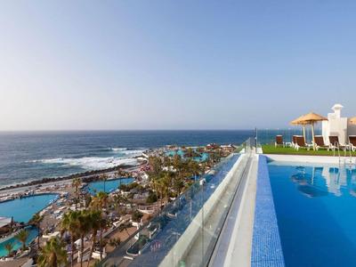 Infinity pool overlooking the sea, beach, and hotel outdoor areas under a clear sky.