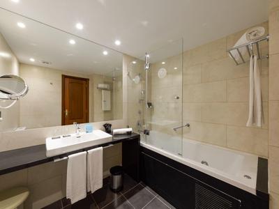 Modern bathroom with bathtub, glass shower, and large mirror in light tones.