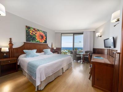 Bright hotel room with double bed, sea view, and modern wooden decor.