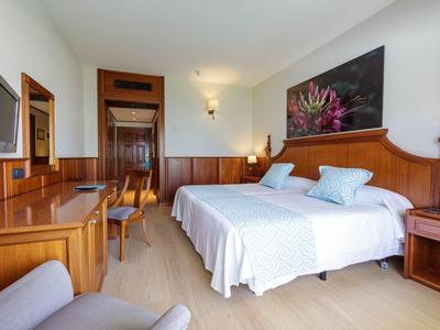 Bright hotel room with a large double bed, wooden furniture, and a flat-screen TV.