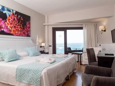 Modern hotel room with double bed, sea view, and cozy seating area.