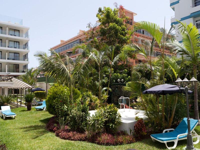 Garden area with loungers, umbrellas, and dense tropical plants next to hotel buildings.
