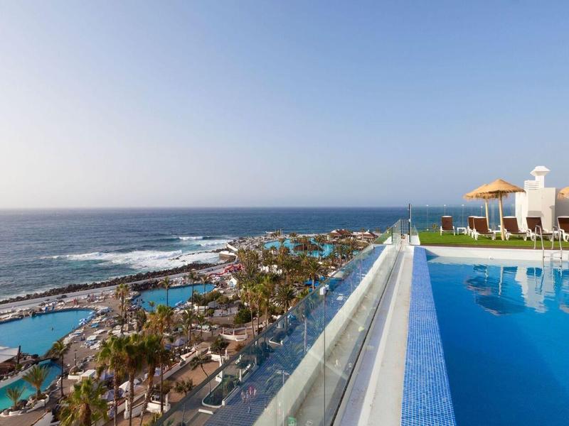 Infinity pool overlooking the sea, beach, and hotel outdoor areas under a clear sky.