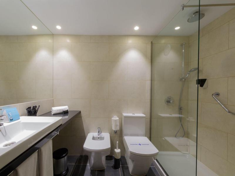 Modern bathroom with double sinks, toilet, bidet, and glass-enclosed shower.
