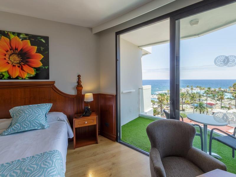 Hotel room with balcony, sea view, single bed, and armchair