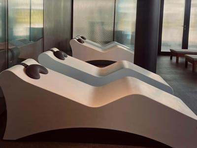 Drei moderne Liegen mit Kopfkissen in einem ruhigen Wellnessbereich mit großen Fenstern.