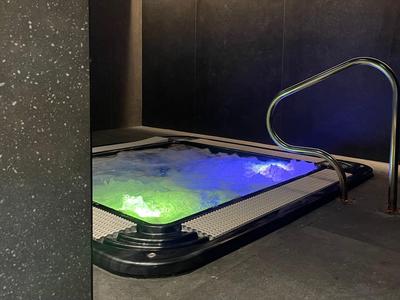 Beleuchteter Whirlpool mit buntem Wasser in dunklem Raum und Edelstahlgeländer