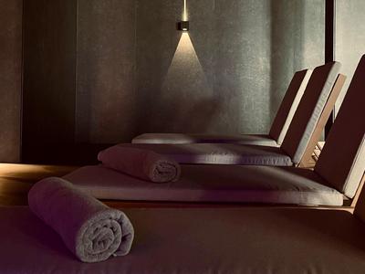 Dunkler Wellnessraum mit Liegen und aufgerollten Handtüchern unter gedämpftem Licht.