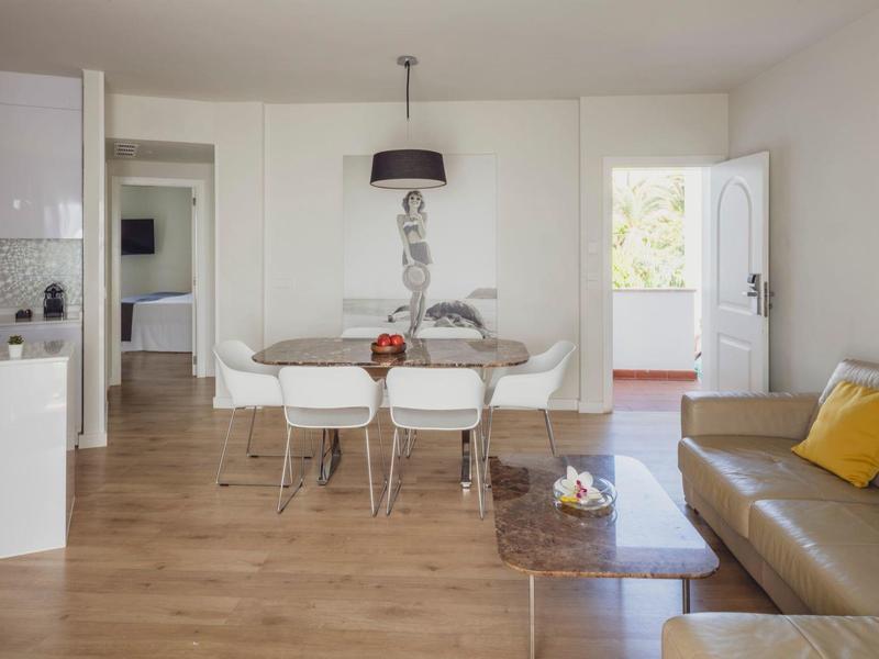 Moderner Ess- und Wohnbereich mit Holzboden, weißem Tisch, Stühlen, brauem Sofa und minimaler Dekoration.