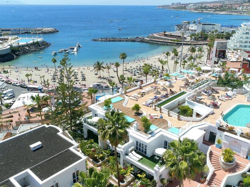 Blick auf Hafen, Strand, Pools und Palmen in einer modernen Küstenstadt bei klarem Wetter.