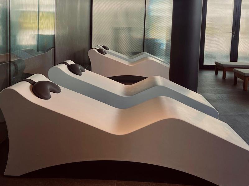 Drei moderne Liegen mit Kopfkissen in einem ruhigen Wellnessbereich mit großen Fenstern.