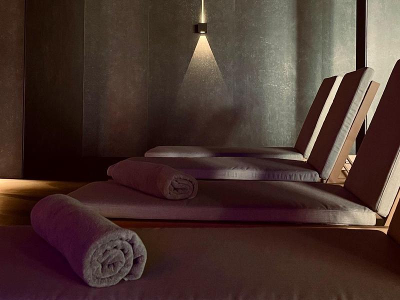 Dunkler Wellnessraum mit Liegen und aufgerollten Handtüchern unter gedämpftem Licht.