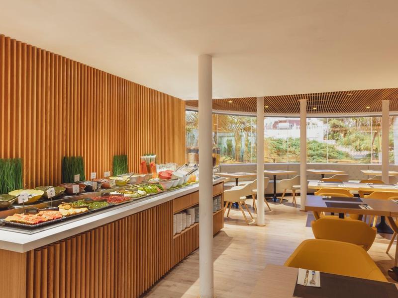 Modernes, helle Buffet mit Holzvertäfelung und Sitzbereich mit gelben Stühlen und großen Fenstern.