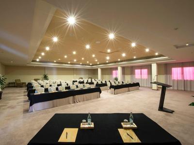 Salle de conférence équipée de chaises, tables et podium sous des lumières vives.