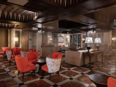 Salon d'hôtel chaleureux avec des fauteuils orange, un sol en marbre à damier et un éclairage doux.