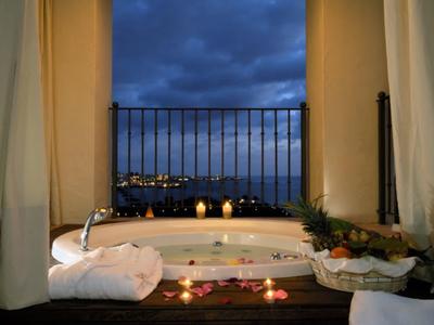 Jacuzzi intérieur confortable avec bougies, serviettes et vue nocturne sur la mer depuis le balcon.