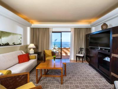 Chambre d'hôtel spacieuse avec canapé, fauteuils, meubles en bois et balcon avec vue sur la mer.