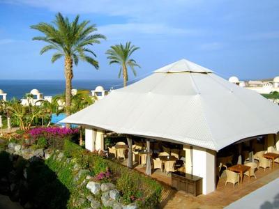 Groot wit zonneschermtent met zithoek en palmbomen nabij de zee.